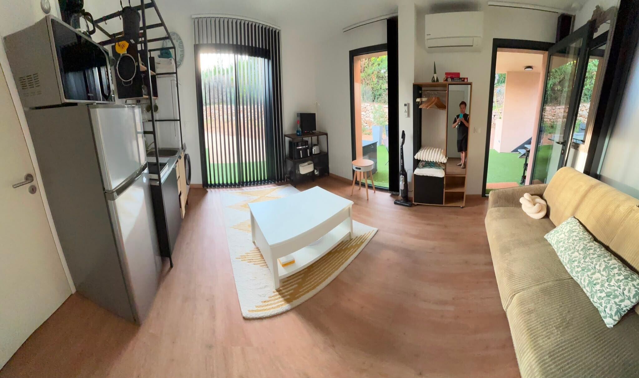 Ein kompakter Wohnbereich mit Küchenzeile, einer Couch, einem kleinen Tisch und einer Schiebetür zu einem Balkon.