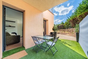 Eine moderne Außenpatio mit einem Glastisch und Stühlen, einem Grill und Blick auf eine natürliche Landschaft.