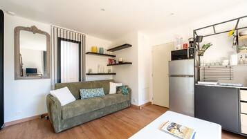A compact living space with a sofa, a dining table, a kitchen area with a refrigerator, and a mirror.