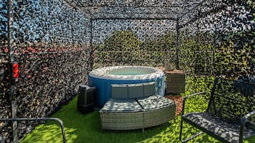 Ein runder Whirlpool, umgeben von einem Zierzaun, mit einer Rasenfläche und Gartenmöbeln.