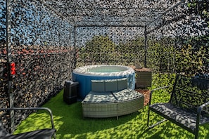 A circular hot tub surrounded by a patterned fence, with a grassy area and outdoor furniture.