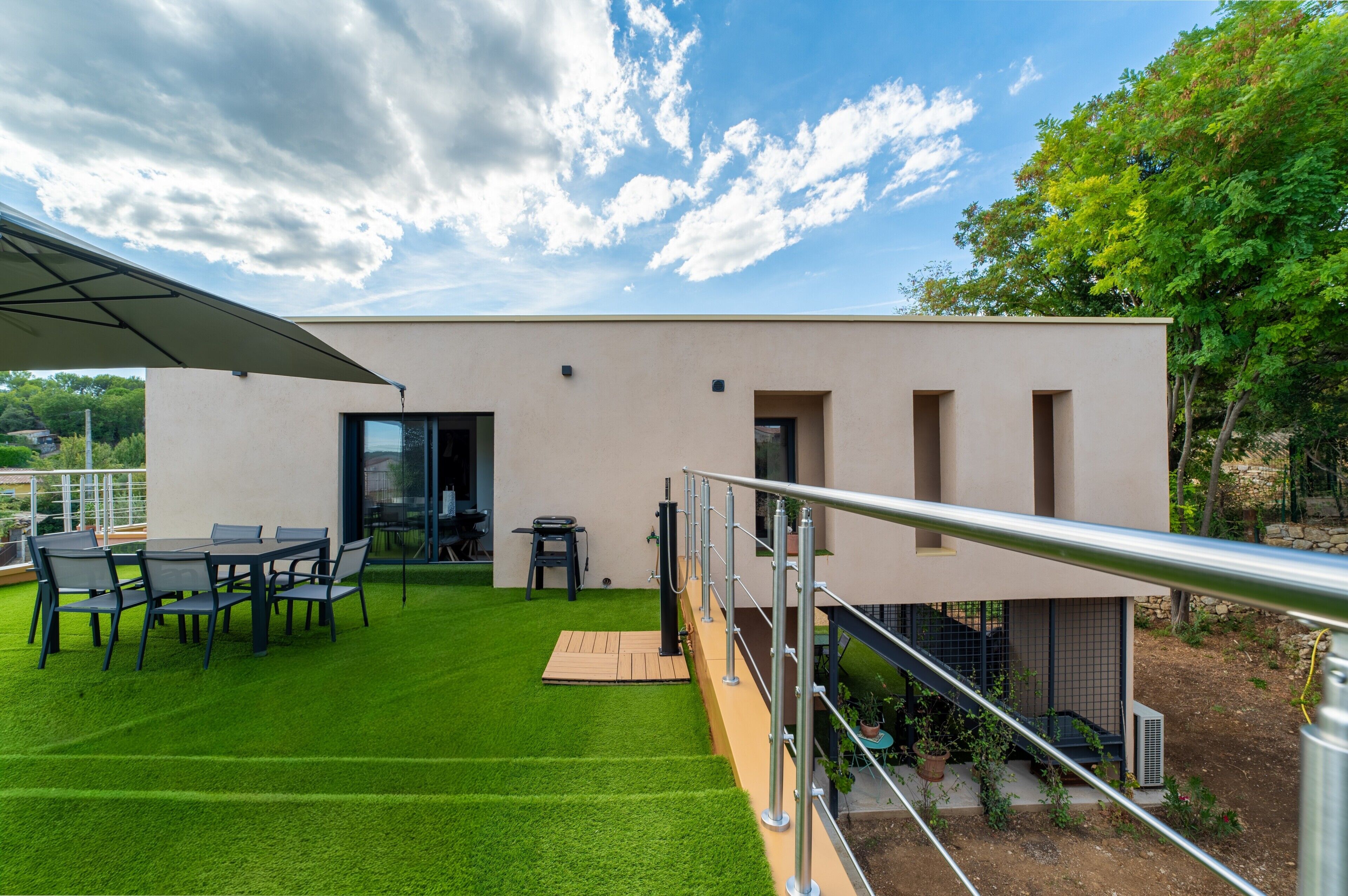 A modern outdoor patio with a dining table and chairs, a barbecue grill, and a staircase leading to an upper level.