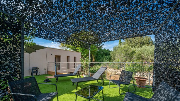 Een overdekt buitengebied met terras, zitplaatsen en uitzicht op een gebouw.