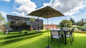 Een terras met een tafel en stoelen, een grote parasol en een muur begroeid met planten.