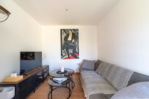 Ein modernes Wohnzimmer mit einem Flachbildfernseher, einem Glastisch, einer Couch und einem Bild an der Wand.