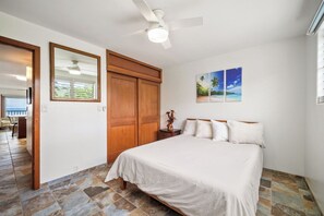 Een slaapkamer met een bed, een plafondventilator, een houten kledingkast en een muur met een ingelijst kunstwerk.