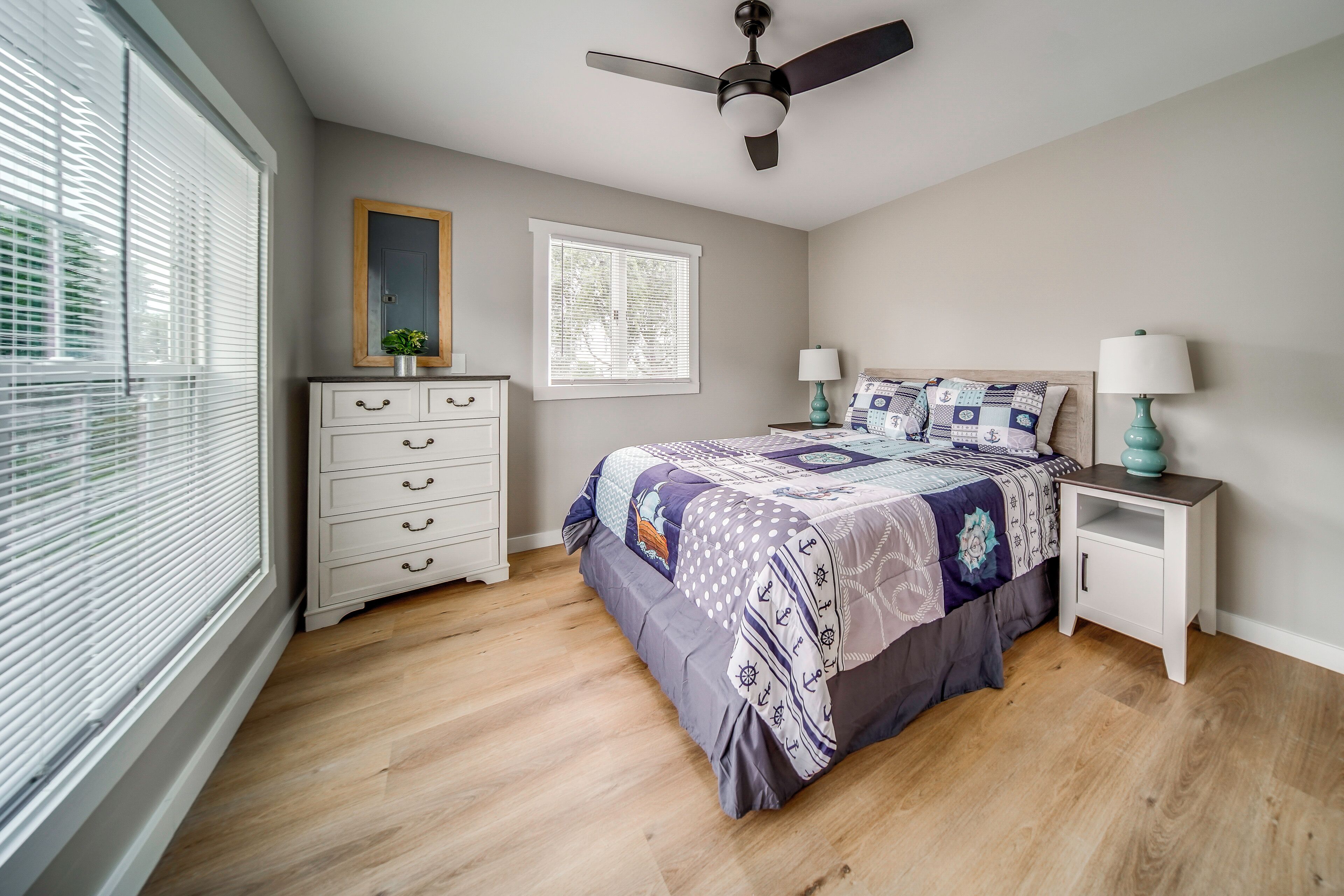 A bedroom with a bed, nightstands, a dresser, a ceiling fan, and a window with blinds.
