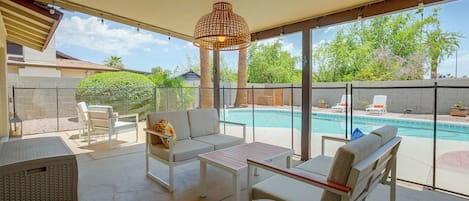 Et overdækket udendørs opholdsområde med swimmingpool, liggestole og et bord.