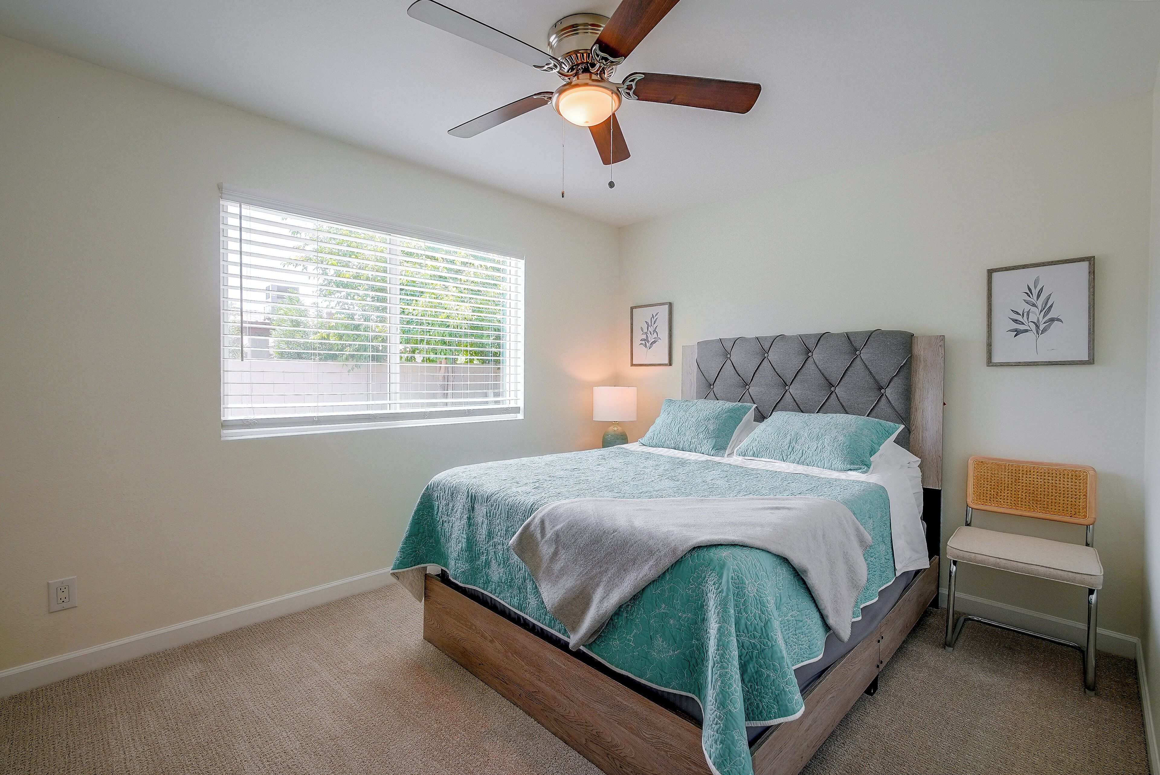 A bedroom with a bed, a ceiling fan, a window with blinds, and a bedside table.