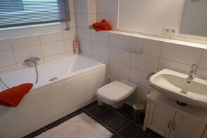 Un baño con bañera, inodoro, lavamanos y una ventana con persianas.