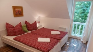 Quarto com duas camas, mesa de cabeceira, abajur e janela com vista para área verde.