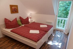 A bedroom with two beds, a nightstand, a lamp, and a window with a view of greenery. - Apartment 4.3 – Holiday apartment in Graal-Müritz (Graal-Müritz)