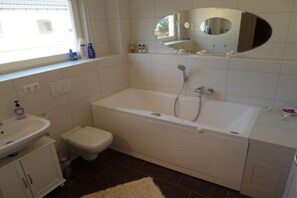 A bathroom with a bathtub, toilet, sink, and a mirror above the sink. - Apartment 4.3 – Holiday apartment in Graal-Müritz (Graal-Müritz)
