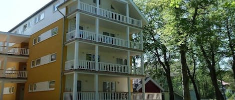 Un immeuble à plusieurs étages doté de balcons, d’un porche couvert et d’une petite construction adjacente.