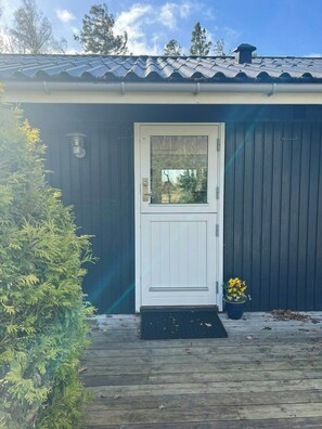 Ein Gebäude mit einer weißen Tür, einer kleinen Veranda und einem Blumentopf mit gelben Blüten.