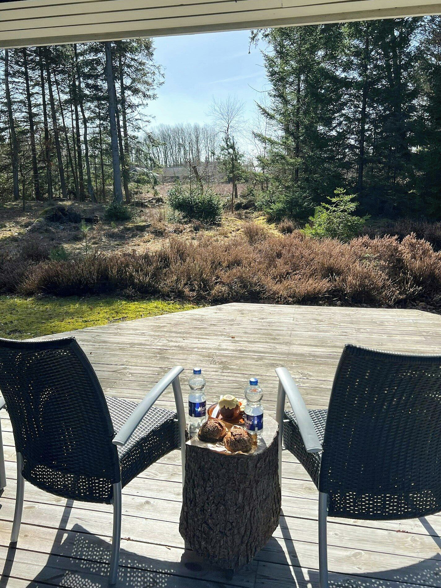 Un espace extérieur aménagé avec deux chaises et une table, une bouteille d’eau et un muffin posés sur une souche d’arbre.