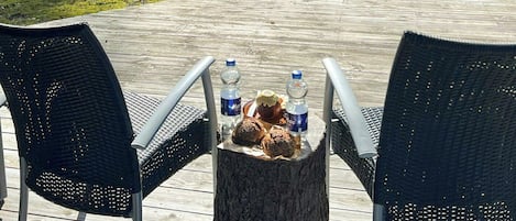 En utomhusplats med två stolar och ett bord, en vattenflaska och en muffin placerad på en trädstam.