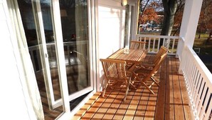 Um deck de madeira com mesa e cadeiras, corrimão branco e porta de vidro que dá para um espaço de pátio.