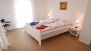 Quarto com cama, mesas de cabeceira, cadeira e escrivaninha.