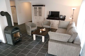 Ein Wohnzimmer mit Kamin, zwei Sesseln, einer Couch, einem Couchtisch, einem Fernseher und einem Schrank.