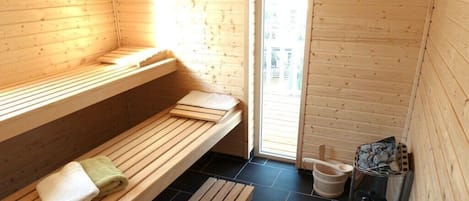 Un sauna avec des bancs en bois, une serviette, un seau et un appareil de chauffage pour sauna.
