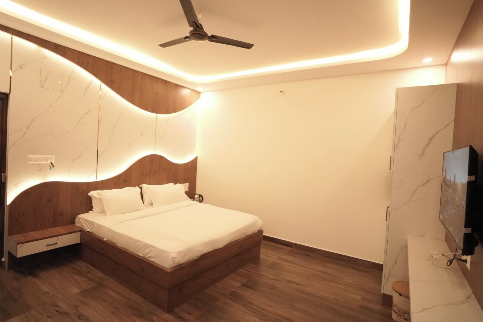 Un dormitorio moderno con estructura de cama de madera, ventilador de techo y pared con diseño de mármol.