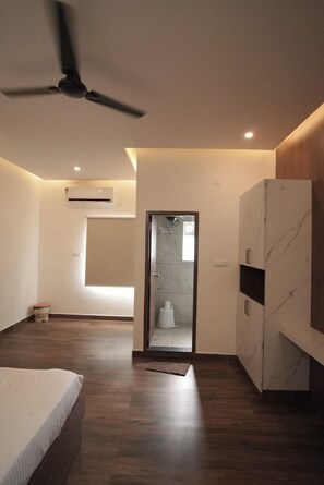 Une chambre moderne avec un lit, un ventilateur de plafond, un appareil de climatisation et une vue sur la salle de bain à travers une porte en verre.