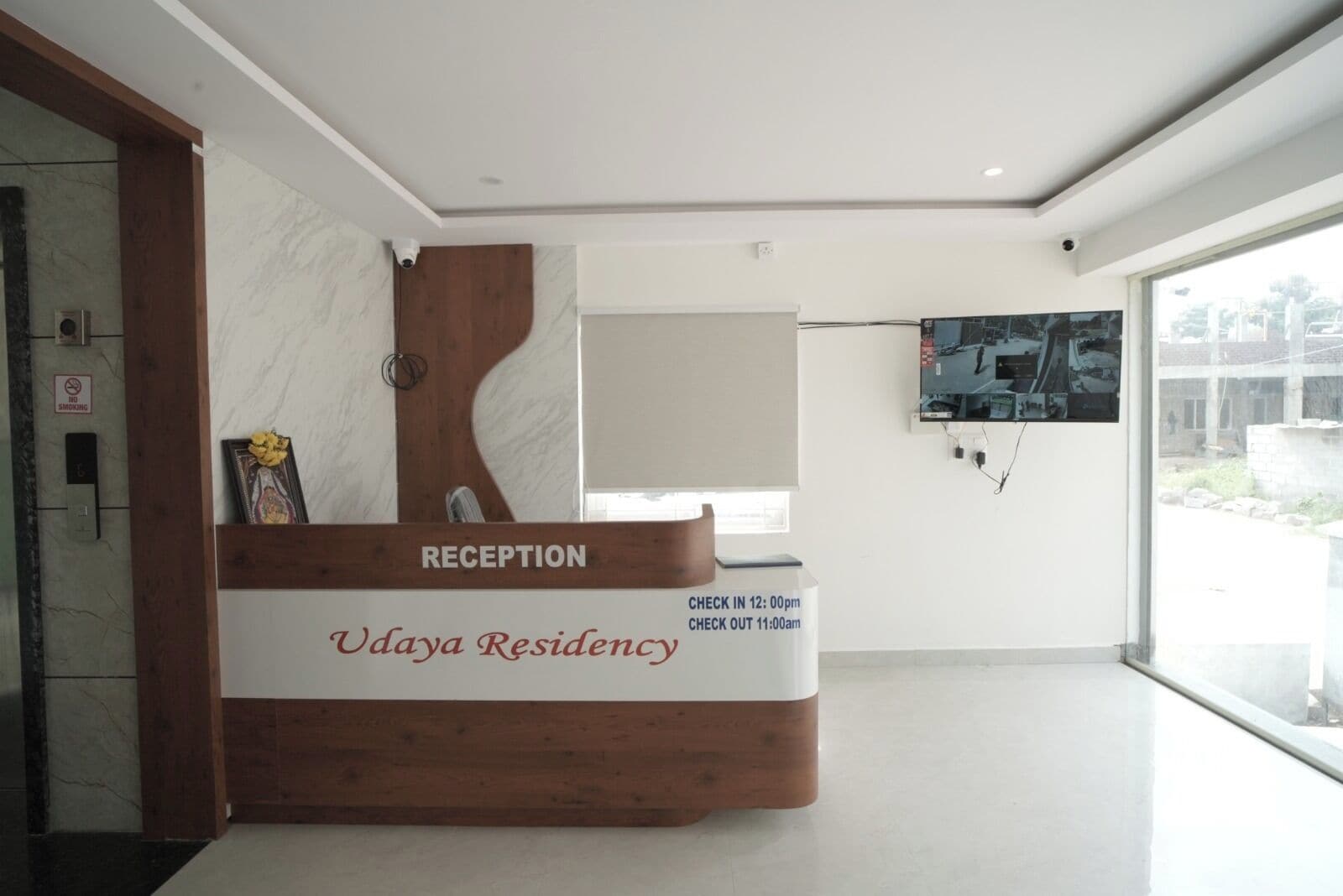A reception desk with a wooden design, a check-in/out schedule, and a view of the outside through a large window.