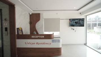 A reception desk with a wooden design, a check-in/out schedule, and a view of the outside through a large window.