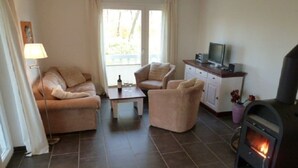 A living room with a sofa, armchair, a small table, a television, and a fireplace. - Holiday apartment with 1 bedroom (Graal-Müritz)