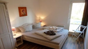 A bedroom with a bed, bedside tables, a nightstand, a chair, and a window. - Holiday apartment with 1 bedroom (Graal-Müritz)