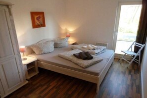 Un dormitorio con cama, mesitas de noche, una silla y un ventanal.