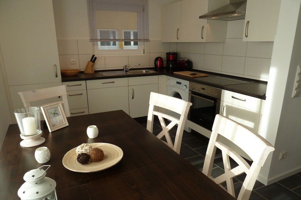 Une cuisine avec des meubles blancs, une table en bois foncé et un lave-linge.