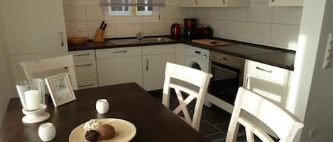 Une cuisine avec des meubles blancs, une table en bois foncé et un lave-linge.