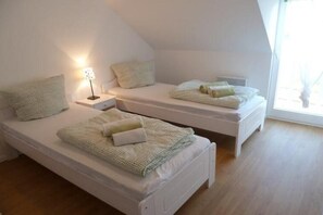 Un dormitorio con dos camas individuales, una mesita de noche con lámpara y una ventana que proporciona luz natural.