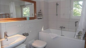 Casa de banho com lavatório, sanita, banheira e janela com vista para árvores.