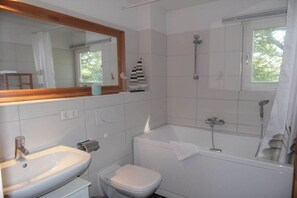 Un baño con lavamanos, inodoro, bañera y ventana con vista a árboles.