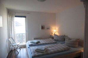 Un dormitorio con dos camas, una ventana con cortinas, una mesita de noche con lámpara y una silla.