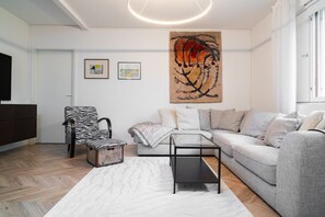 Een moderne woonkamer met een grijze bank, een stoel met zebraprint, een glazen salontafel en een groot abstract schilderij aan de muur.