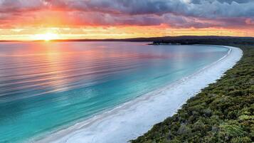 A coastal landscape with a beach, clear water, and a sunset.
