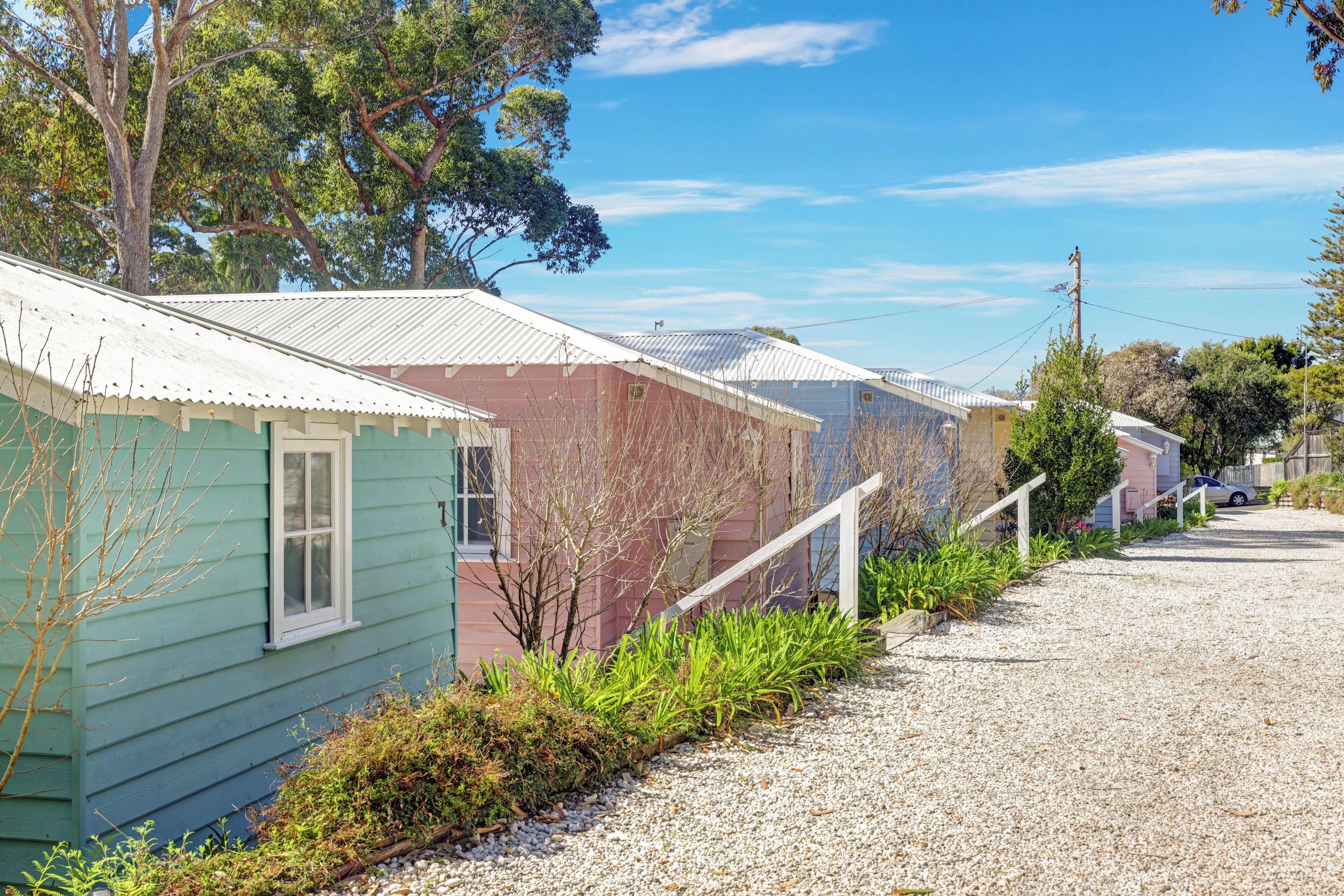A row of single-story houses with metal roofs, a gravel driveway, and a clear sky.