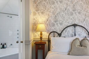 Una habitación de hotel con cama, mesita de noche, lámpara y ducha.
