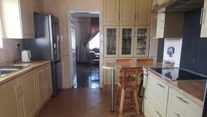 A kitchen with a refrigerator, stove, sink, and wooden chairs.