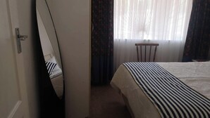 A bedroom with a bed, a mirror, a chair, and a window with curtains.