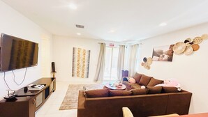 A living room with a sofa, television, and a dining area with a table. - Spacious 4BR Tolleson Retreat ; Office, Patio & BBQ ;Phoenix west valley (Tolleson)