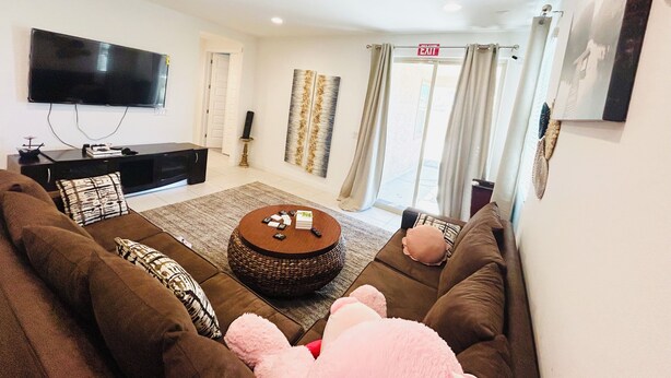 A living room with a large flat-screen TV, a sofa set, a coffee table, and a door leading to an outdoor area. - Spacious 4BR Tolleson Retreat ; Office, Patio & BBQ ;Phoenix west valley (Tolleson)