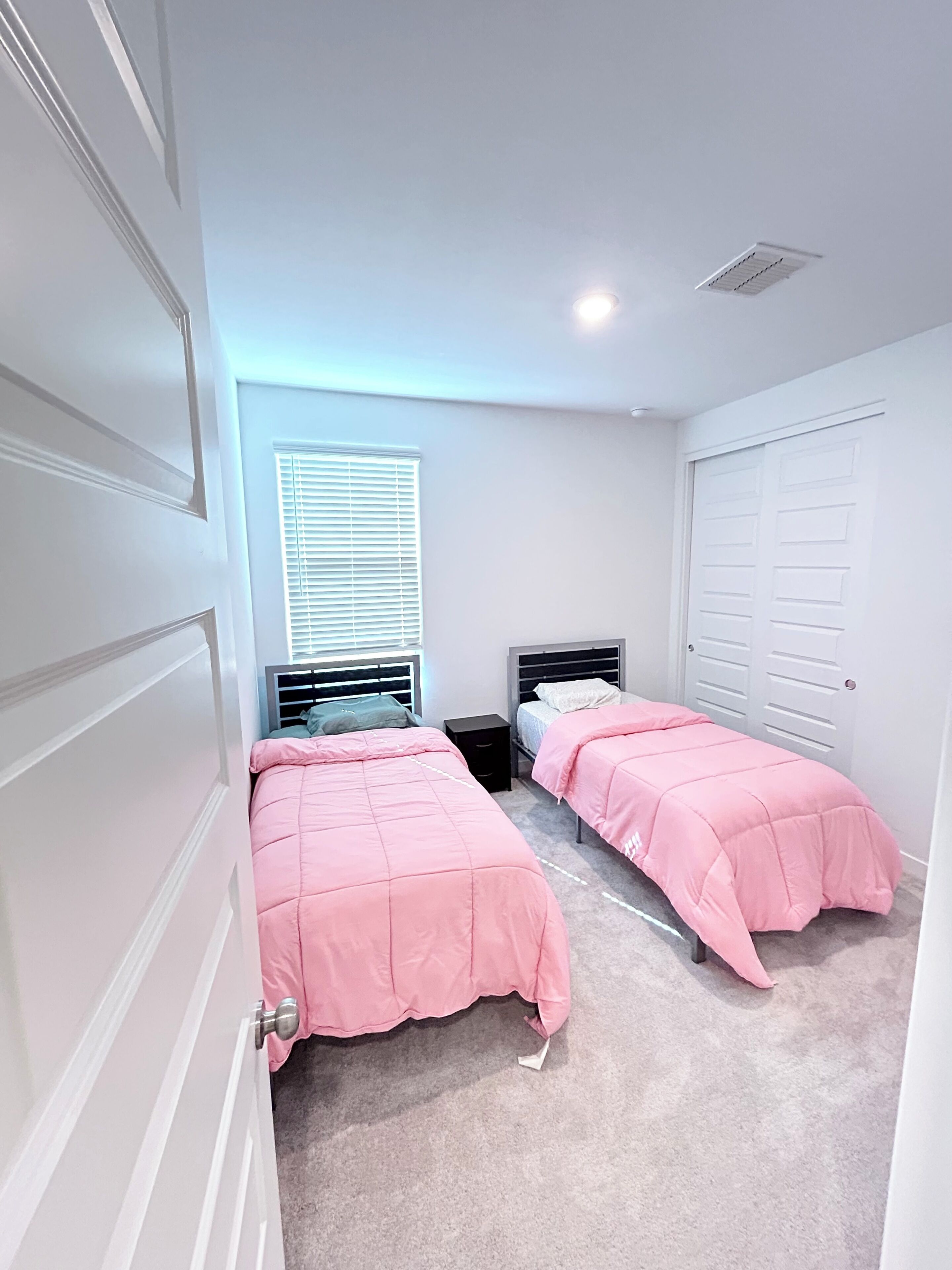 Une chambre avec deux lits, une fenêtre avec des stores, un placard et une porte.