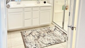 A modern bathroom with a large mirror, white cabinetry, a shower enclosure, and a patterned rug. - Spacious 4BR Tolleson Retreat ; Office, Patio & BBQ ;Phoenix west valley (Tolleson)