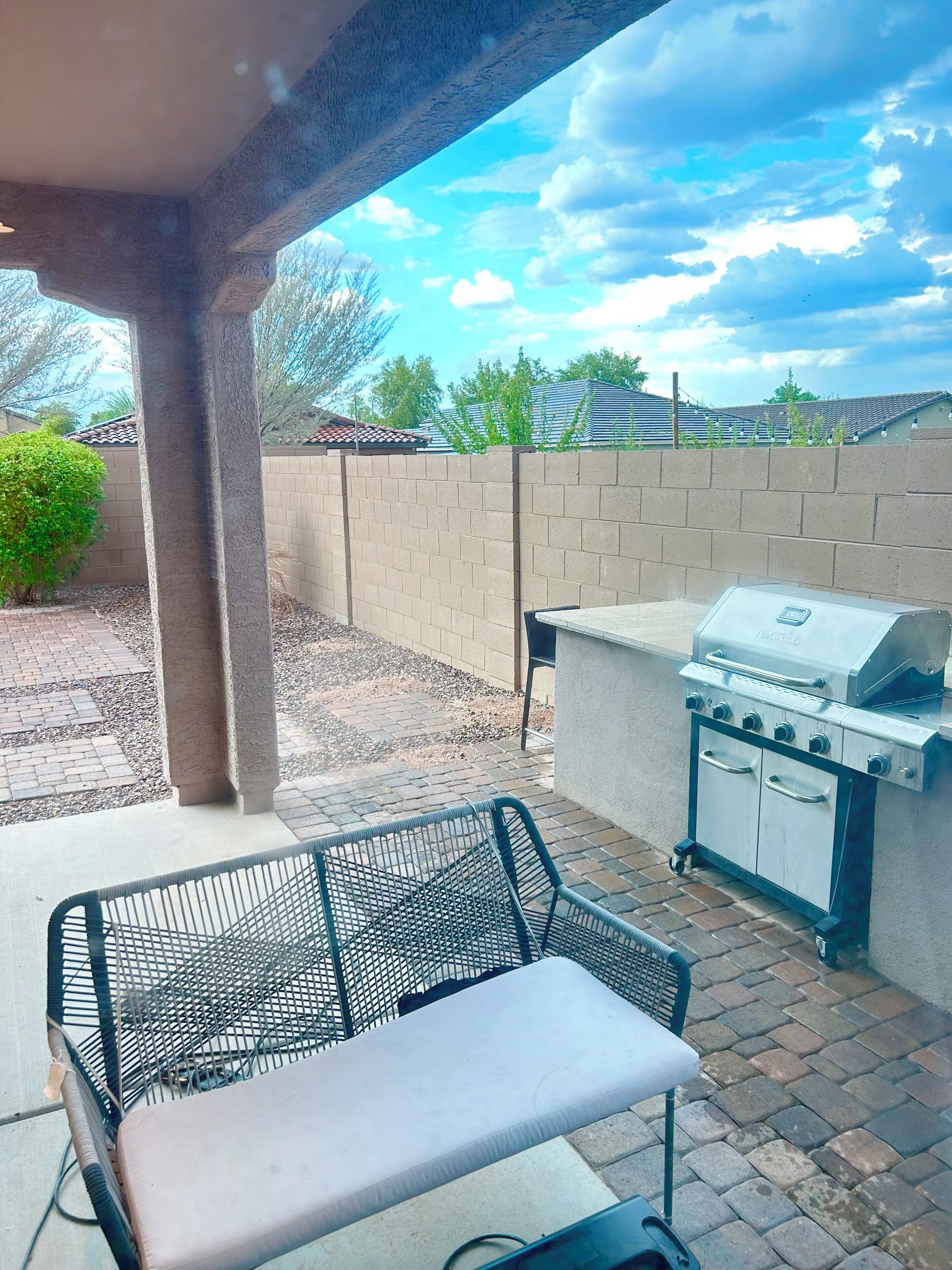 Une terrasse extérieure avec un barbecue, une chaise en métal et un mur en briques.