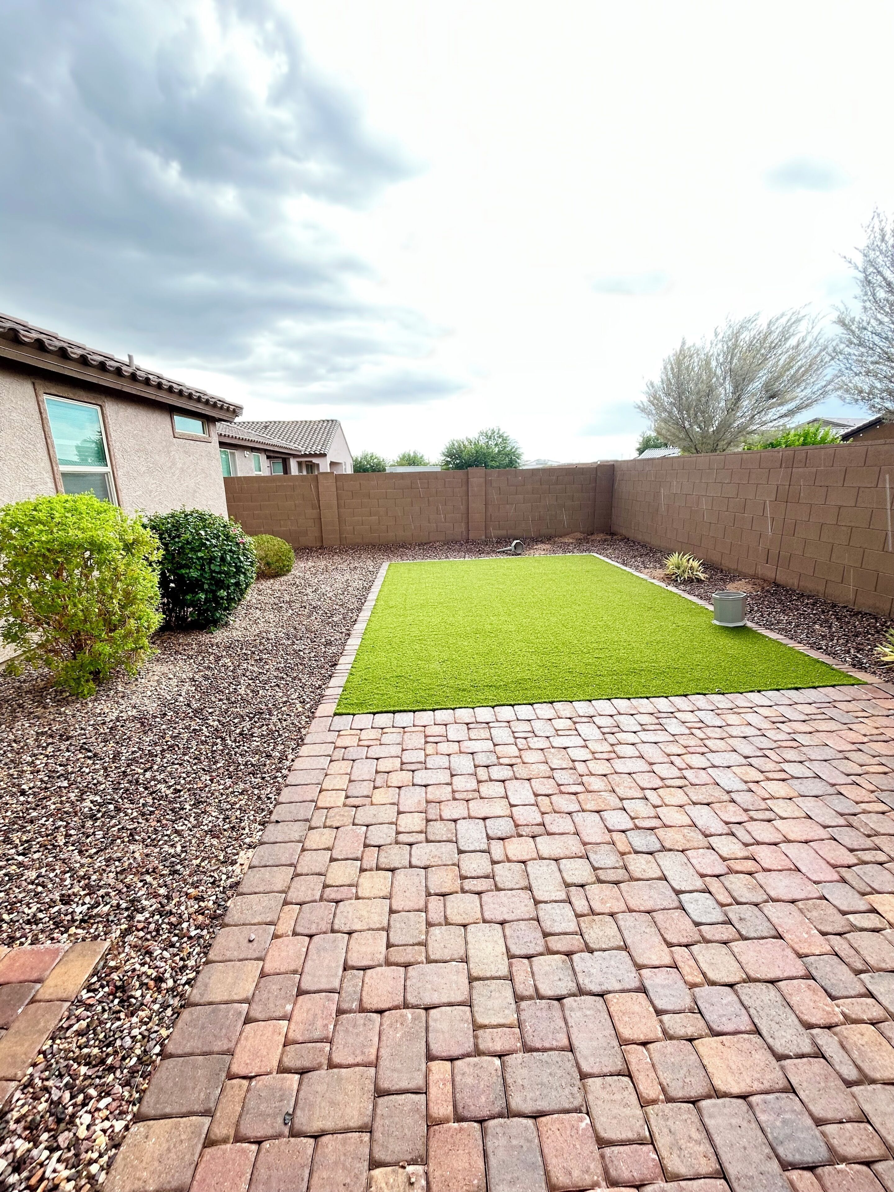 Un jardin avec une terrasse dallée, une pelouse et un mur en briques.